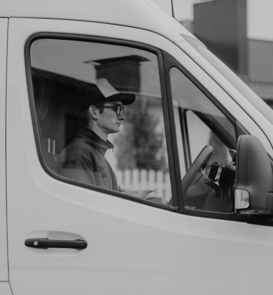 Black and white image of a delivery driver inside a cargo van, showcasing service and transportation.